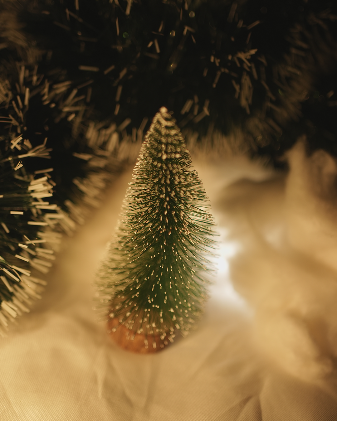 Small Christmas tree with gold tinsel and warm lights on a snowy background.