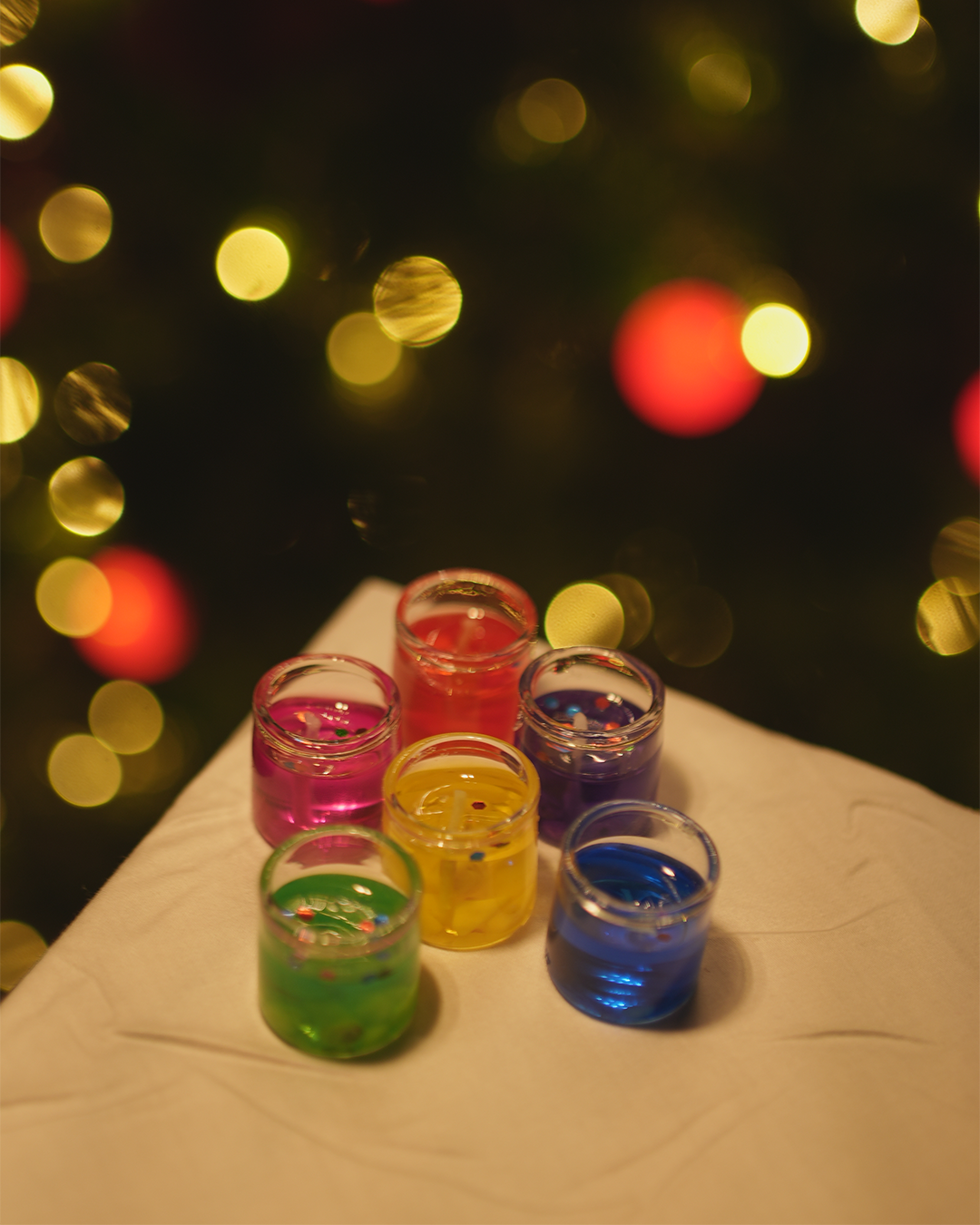 Colorful votive candles or wax melts, with a festive bokeh background.