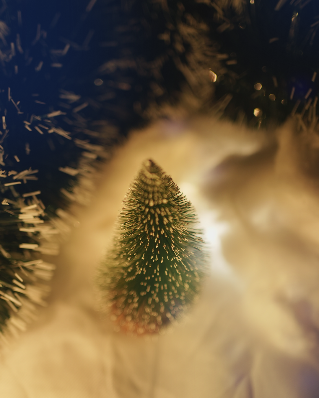 Miniature Christmas tree with gold tinsel on a sparkling background.