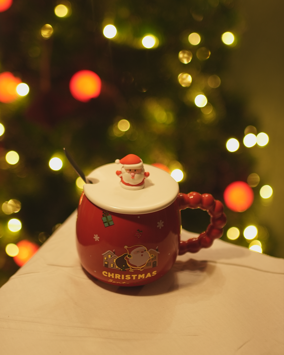 Ceramic Christmas mug with lid, spoon, and holiday design. Perfect for warm drinks!