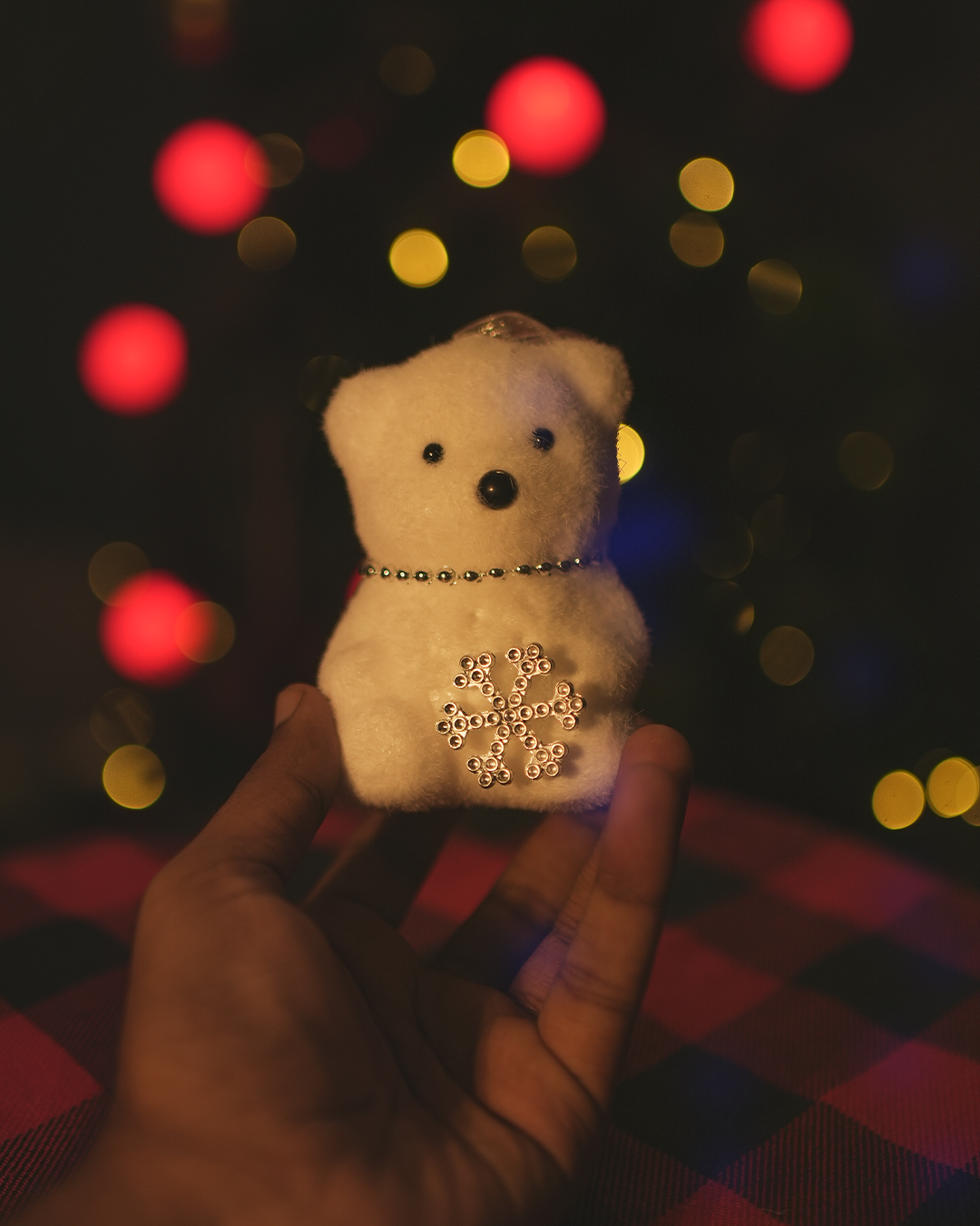 Hand holding a cute Christmas bear ornament with festive bokeh background.