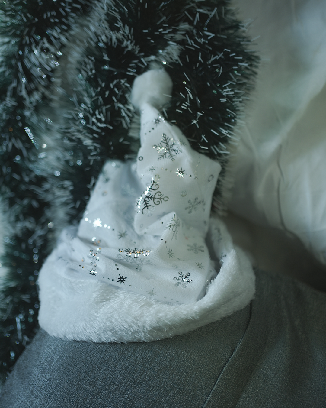 Close-up of a white Christmas plush hat with silver snowflakes resting on a festive green garland.
