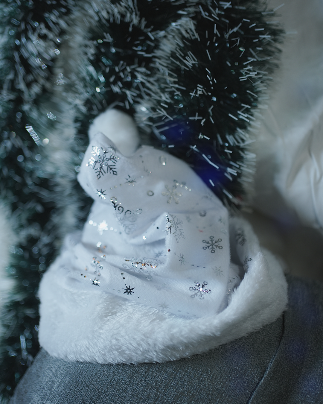 White plush Christmas hat with silver snowflakes resting on tinsel.